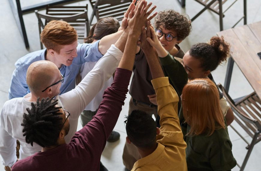A diverse group of professionals high-fiving in a modern office, showcasing teamwork and collaboration.