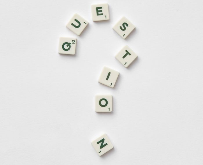 Artistic arrangement of letter tiles forming a question mark on a white background.